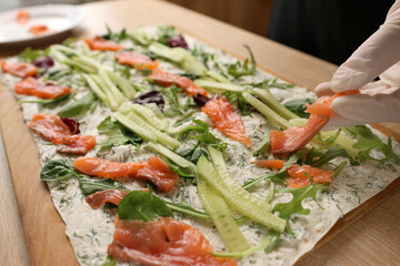 Salmon and cucumbers are added to lavash with cheese and greens. Preparation of a roll with cheese,...