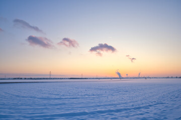 Snowy landscape at sunset, smoking industrial chimneys in the background
