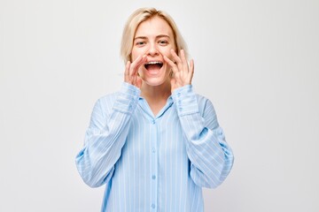 Portrait of blonde girl shouting loudly with hands, news, palms folded like megaphone isolated on...
