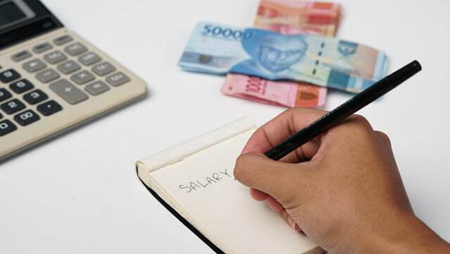 photo of a notebook, calculator, and rupiah banknotes on a white background