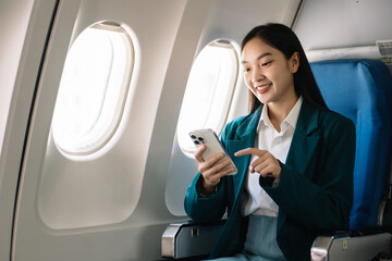 Fototapeta premium Attractive Asian female passenger of airplane sitting in comfortable seat while working laptop and tablet with mock up area using wireless connection.