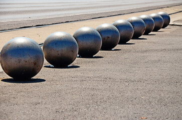 Line of iron spheres on a sunlit street, forming a rhythmic urban pattern with artistic and architectural elements. Captured in strong natural light, the composition combines geometry, shadow play.