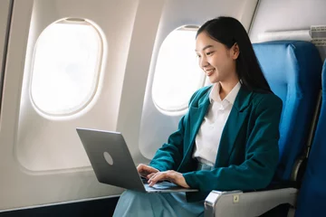 Foto op Canvas Attractive Asian female passenger of airplane sitting in comfortable seat while working laptop and tablet with mock up area using wireless connection. © laddawan