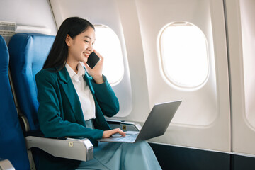 Fototapeta premium Attractive Asian female passenger of airplane sitting in comfortable seat while working laptop and tablet with mock up area using wireless connection.