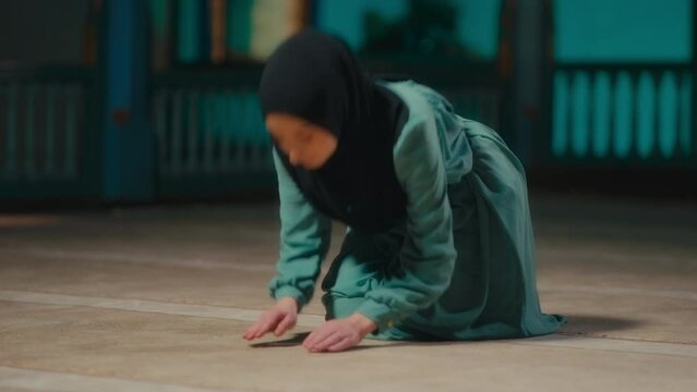Young Muslim Woman with a Headscarf Bowing in a Prayer in the Mosque at Night