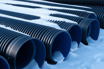 Plastic black corrugated drainage pipes are neatly arranged on the snowy surface during the winter. - obrazy, fototapety, plakaty