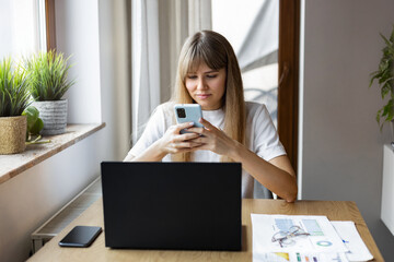 Modern young business woman freelancer working using laptop, engaged in remote work sitting at home at the table