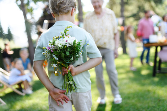 Beautiful senior birthday woman receiving flowers from grandchildren. Concept of garden birthday party for elderly woman.