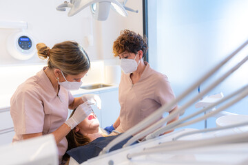 Dentist and assistant performing a mouth and teeth check on a client in the modern dental clinic