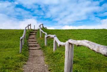 Endless small path with stairs in green meadow framed by wooden fence. Thougthful scene against blue sky. Shallow depth of field with focus on stairs.