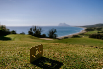 Sotogrande, Spain - January, 23, 2024 - A golf course tee marker in the foreground with a blurred panoramic coastal view and Gibraltar in the background.