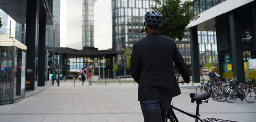 Fototapeta premium Rear view of city bike commuter leaving work on bicycle after long work day. Banner with copy space.