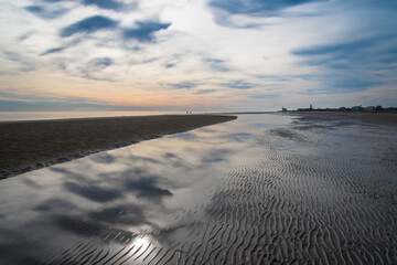 Il cielo e le nuvole del tramonto si riflettono sull'acqua lungo la spiaggia di Caorle, cittadina di mare vicino a Venezia