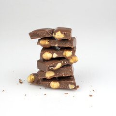 Broken milk chocolate bars with nuts stacked as heap or pile on grey background