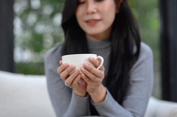 Selective focus of relaxed happy young woman's hands holding coffee cup on sofa at home Smiling girl on holiday