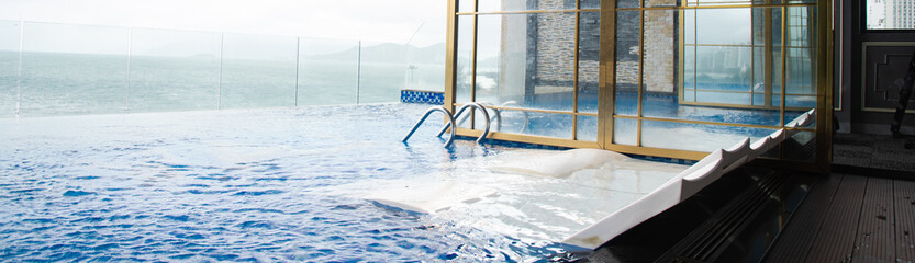 Panorama Infinity pool with white float lounge chairs, handrail, glass wall, ocean and mountain...