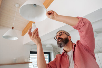 Man changing LED bulbs at home. Concept of energy efficiency, longevitiy and environmental impact of electronic bulb. - obrazy, fototapety, plakaty