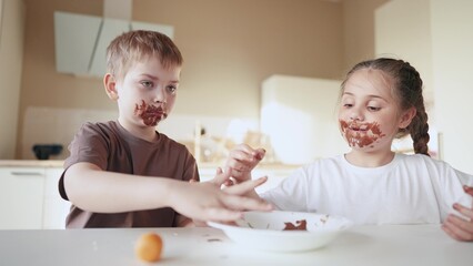 Obraz na płótnie Canvas baby boy and girl eat chocolate. dirty little baby kids in the kitchen eating chocolate in the morning. happy family eating sweets kid dream concept. baby dirty face eating chocolate cocoa sweet