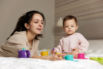 mother and little child daughter playing tea party and spending time together in bedroom, family having fun,
