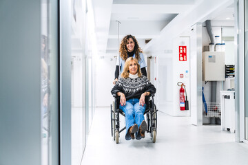 A front view of a dedicated nurse pushing a patient in a wheelchair, moving through a corridor with...