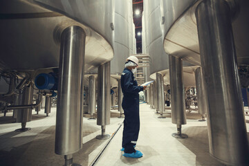 Fototapeta premium Male worker inspection a record process milk cellar at the with vertical stainless steel tank