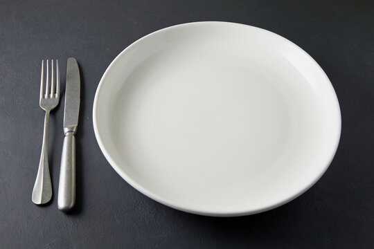 White plate with cutlery on a black concrete table. Food display template