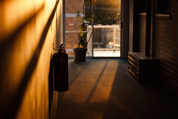 Silhouette of fire extinguisher in motel hallway illuminated by golden afternoon sunlight