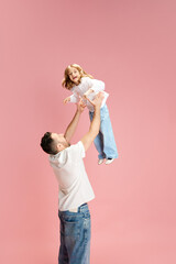 Have fun together. Man lifting laughing child in air with joyful expression against pink pastel background. Concept of International Day of Happiness, childhood and parenthood, positive emotions. Ad