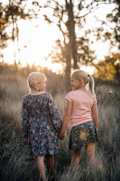 2 young girls holding hands looking at each other as they walk away