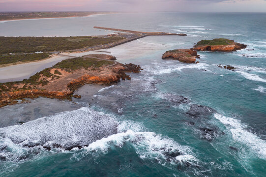 Aerial view of waves crashing against islands along a rugged coastline in bad weather