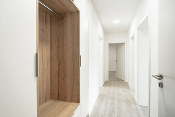 A Clean, modern hallway with wooden floors, white walls, an open wooden closet, and opened doors....