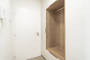 A Minimalist room with a white door, an intercom, and a built-in wooden closet. The room has a...