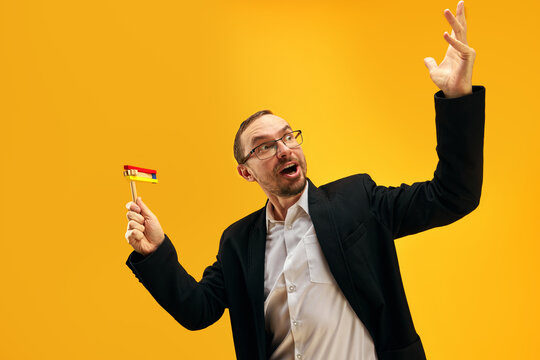 Jewish man in his 30s, in glasses, yarmulke joyfully posing with wooden noisemaker, gragger against yellow studio background. Concept of Purim holiday, Jewish traditions, history and culture
