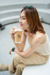 Beautiful trendy hipster asian woman drinkking ice coffee sitting in modern city cafe smiling woman
