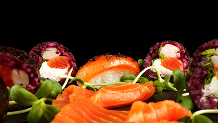 Variety of bright sushi rolls with greens on a black background. Incredible fresh sushi rolls on a dark background. Cooking traditional Japanese seafood and fish dishes.