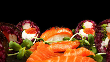 Variety of bright sushi rolls with greens on a black background. Incredible fresh sushi rolls on a dark background. Cooking traditional Japanese seafood and fish dishes.