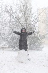 a girl is playing with snow on the street, it is snowing, a blizzard and frost on a winter day