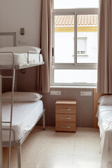 A clean and minimalistic hostel room with a bunk bed, white bedding, and a small wooden bedside...