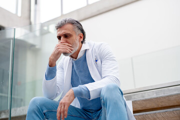 Serious and frustrated male doctor sitting on the stairs. Burnout for healthcare workers.