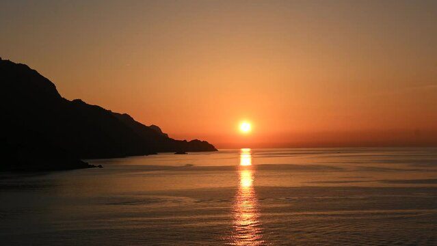 Colorful orange sunset over flat calm water in the Mediterranean Sea by the coast of Corsica