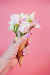 Close-up shot of a woman hand holds waffle cone with pink and white flowers.