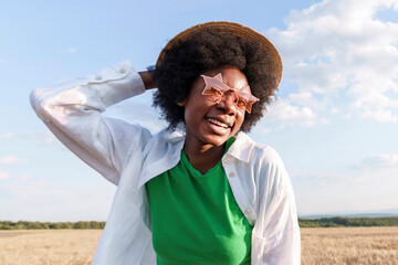 Happy afro woman wearing hat and star shape sunglasses in field