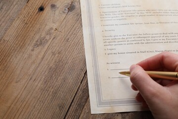 Woman signing Last Will and Testament at wooden table, closeup. Space for text