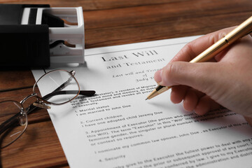 Woman signing Last Will and Testament at wooden table, closeup