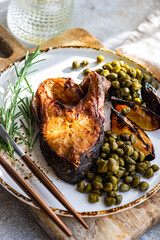 Close-up of a barbecued salmon steak seasoned with spices served with roasted lemon slices and capers garnished with rosemary