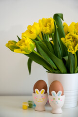 Eggs in bunny shaped egg cups near bunch of yellow tulips