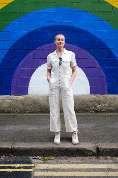 Confident non binary person standing on footpath in front of wall