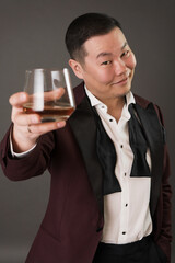 Asian man in a classic suit with a bow tie posing holding a glass of whiskey in his hand