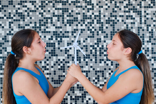 Girls blowing on wind turbine model in front of wall