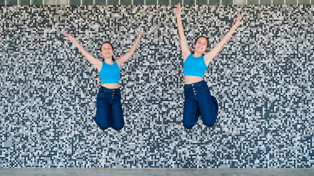 Happy sisters jumping in front of textured wall